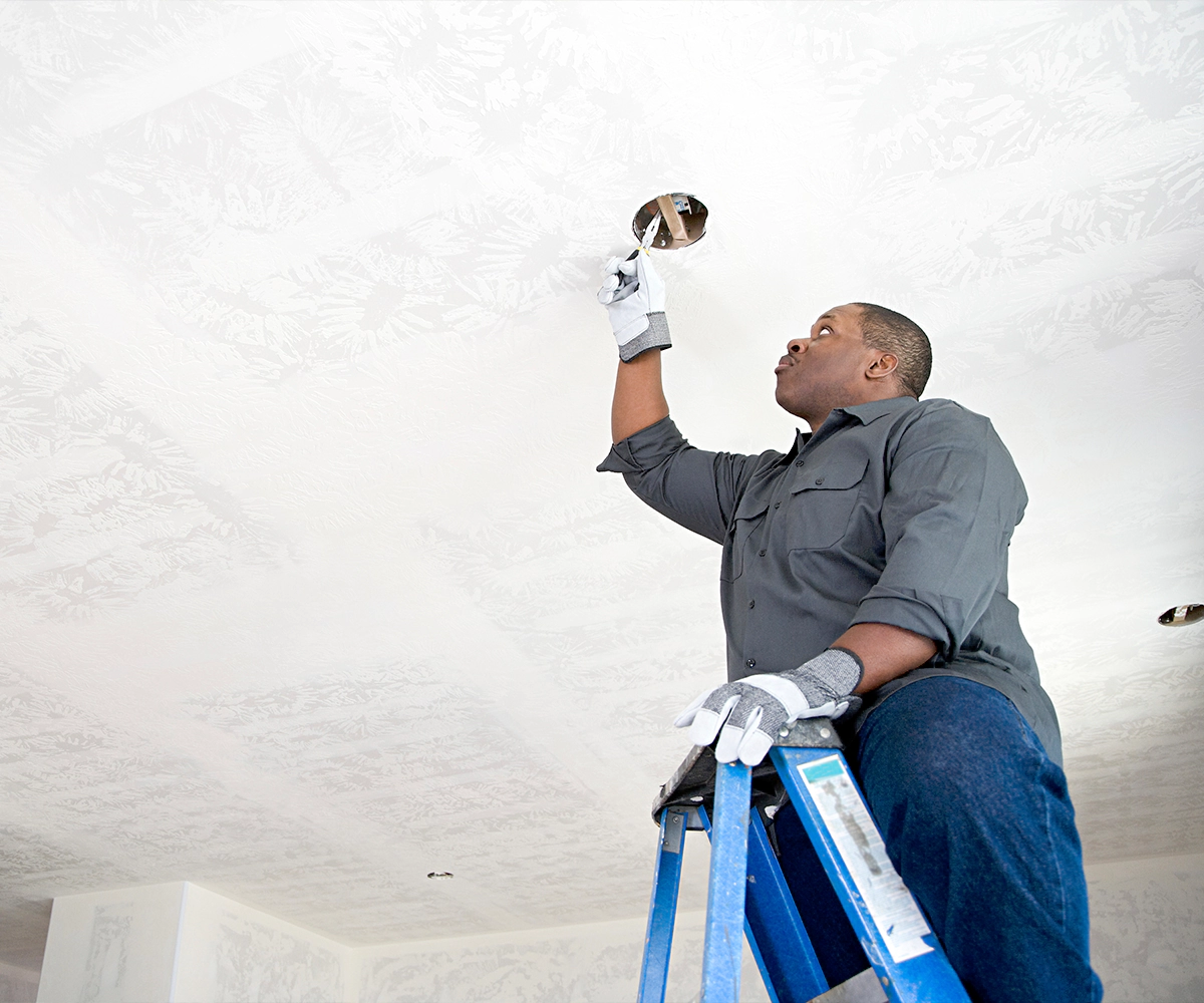 A man on a ladder looking at the ceiling