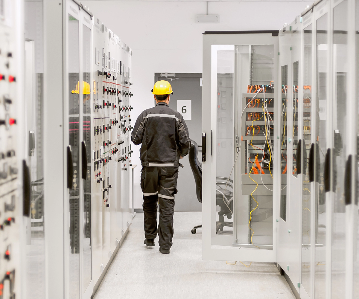 A man in black jacket and yellow hard hat walking through a room.