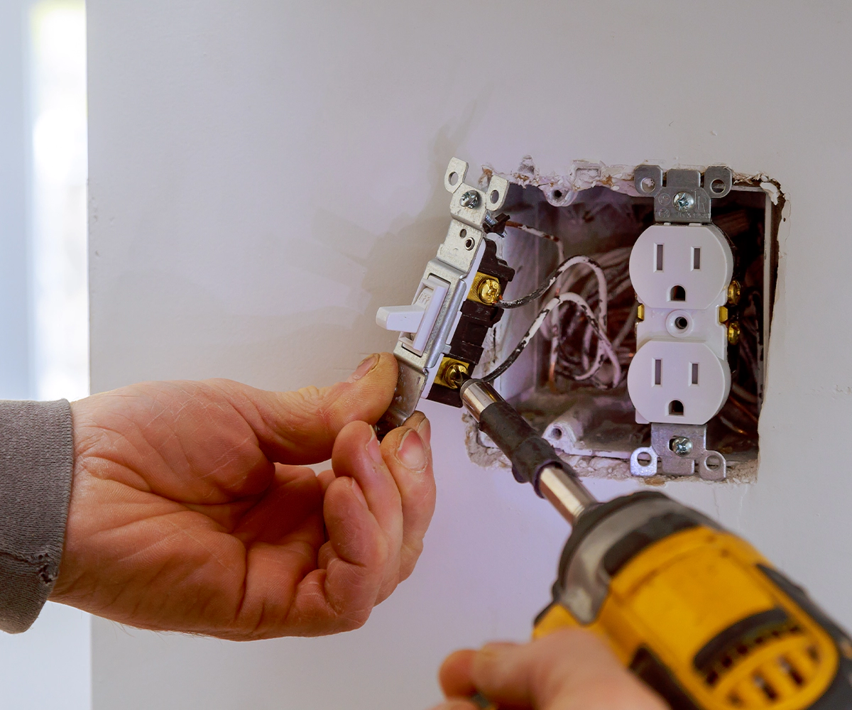 A person using a drill to install an electrical outlet.