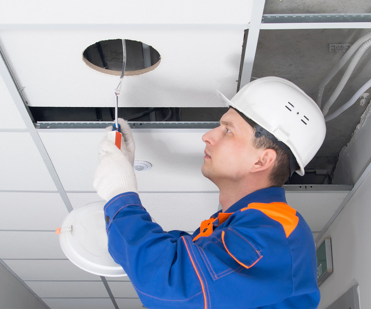 A man in blue work suit and white hard hat working on ceiling.