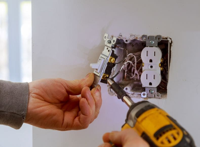 A person using an electric drill to install electrical outlets.