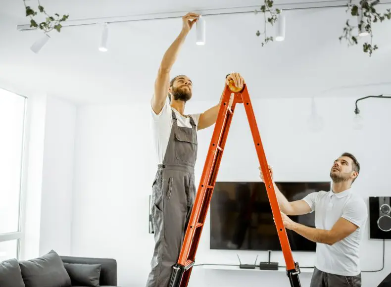 Two men are working on a light fixture.